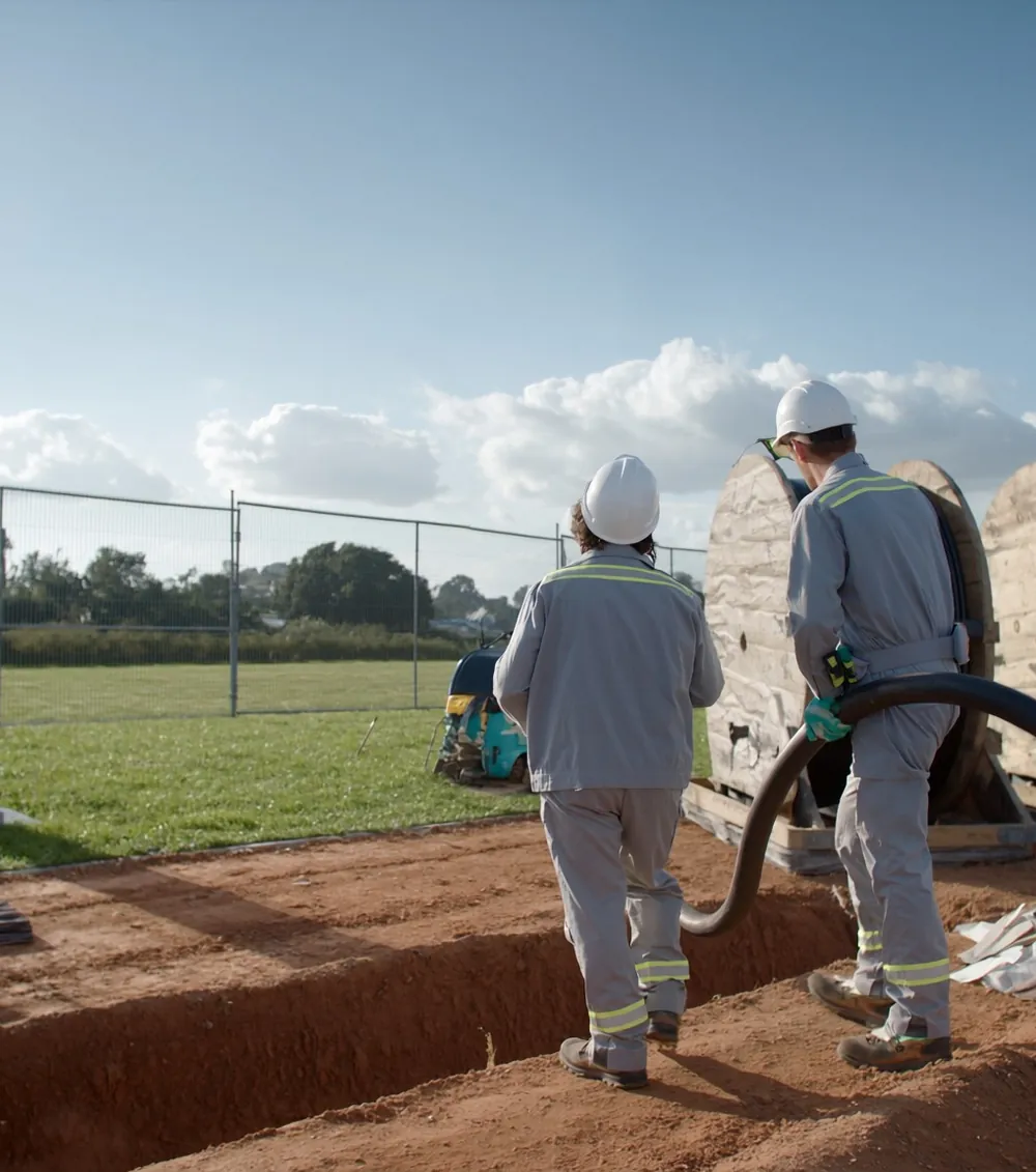 Zwei Arbeiter verlegen Stromkabel in einem Graben auf einer Ladepark-Baustelle